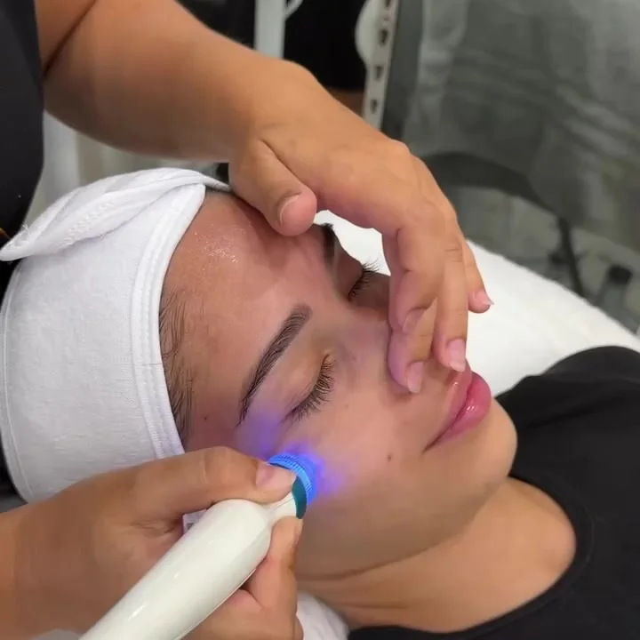 Passage d'un appareil de soin sur le visage d'une cliente, en cabine